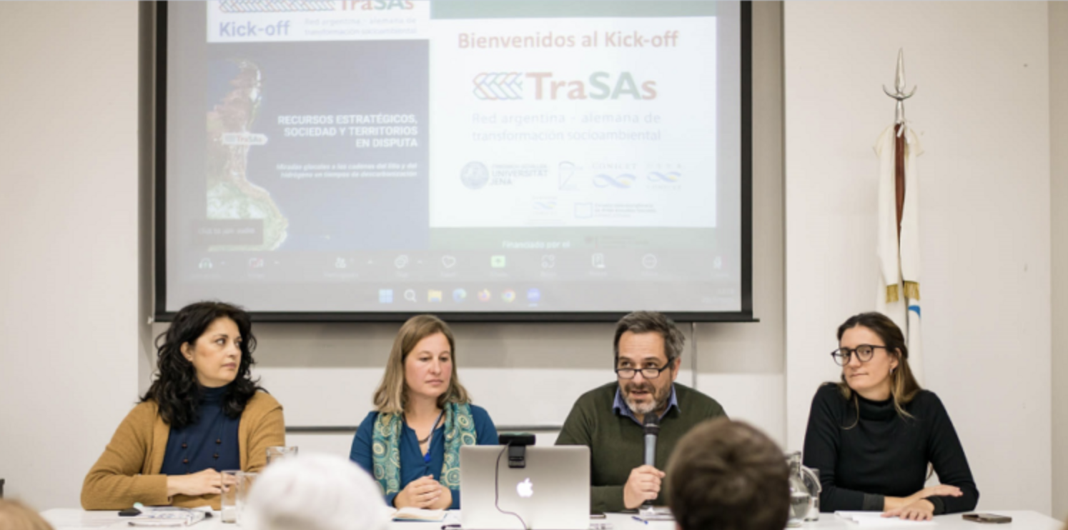 Claudia Tomadoni, Anne Tittor, Pablo Lavarello y Regina Vidosa están sentados en una mesa. Atrás se ve en una pantalle una powerpoint sobre la Red TraSAs. Pablo está hablando en un micrófono, los demás están escuchando.